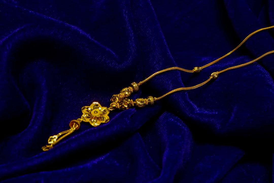 Delicate gold necklace with intricate floral pendant and bead details, displayed elegantly on deep blue velvet fabric, highlighting its luxurious craftsmanship and ornamental beauty.